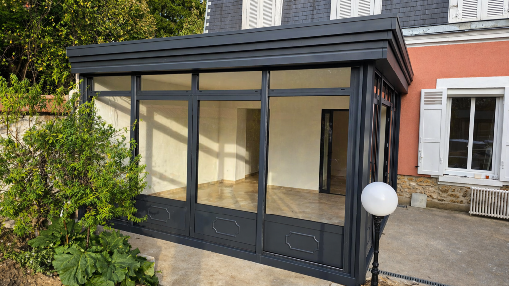 Vue extérieure d’une véranda aluminium gris RAL 7016 granité avec grandes parties vitrées et soubassements assortis.